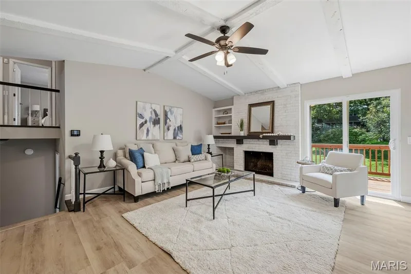 Spacious living room with vaulted ceiling, exposed beams, wood burning fireplace, ceiling fan with light, and LVP flooring. — 3034 Willow Wood Drive, St Charles, MO 63303