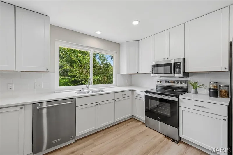 Updated kitchen features 42 inch white cabinetry, granite countertops, breakfast bar, stainless steel appliances, coffee bar, built in pantry, and LVP flooring. — 3034 Willow Wood Drive, St Charles, MO 63303