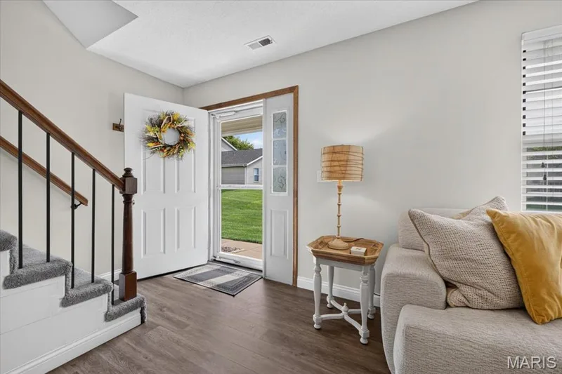 Wood-finish flooring, staircase with carpeted treads and wrought iron balusters, white paneled entry door, sidelight window, and white interior walls — 1383 Forest Creek Drive #5, St Charles, MO 63303