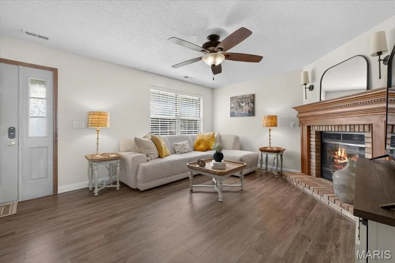 Wood-finish flooring throughout, a wood-mantel fireplace with brick surround, a ceiling fan, and a window with blinds — 1383 Forest Creek Drive #5, St Charles, MO 63303