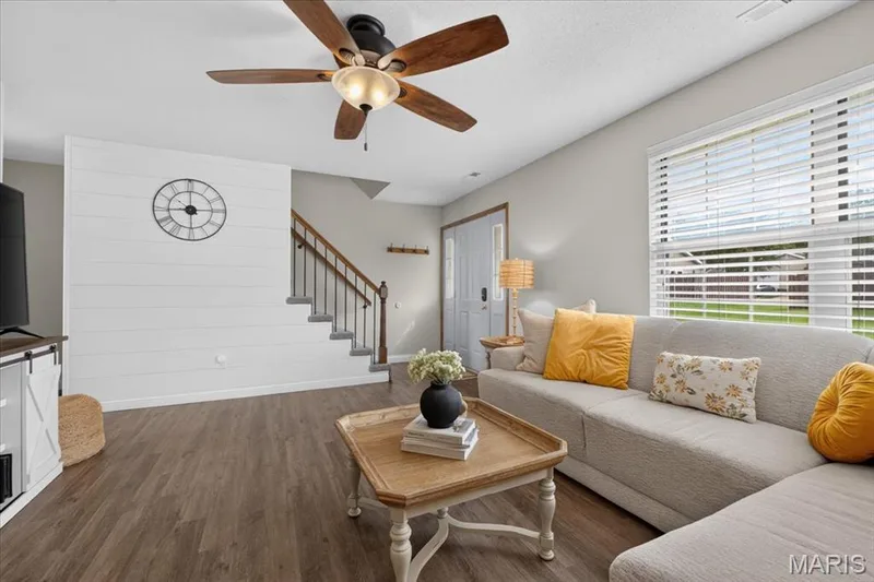 Wood-finish flooring, ceiling fan, white shiplap accent wall, light gray wall paint, and a staircase with dark wood railings — 1383 Forest Creek Drive #5, St Charles, MO 63303