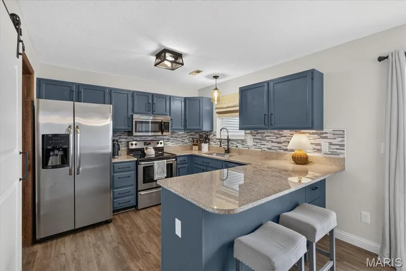 Kitchen featuring wood-finish flooring, stainless steel appliances, blue cabinetry, mosaic tile backsplash, and a peninsula with countertop seating — 1383 Forest Creek Drive #5, St Charles, MO 63303