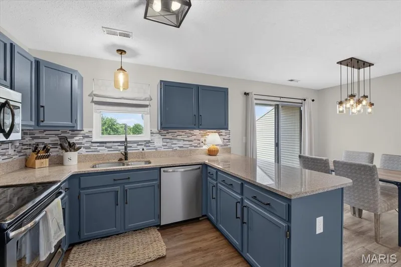 Kitchen featuring blue cabinetry, light-toned countertops, a mosaic tile backsplash, and stainless steel appliances — 1383 Forest Creek Drive #5, St Charles, MO 63303