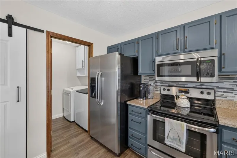 Kitchen featuring blue cabinetry, stainless steel appliances, granite-style countertops, and a gray-toned tile backsplash — 1383 Forest Creek Drive #5, St Charles, MO 63303