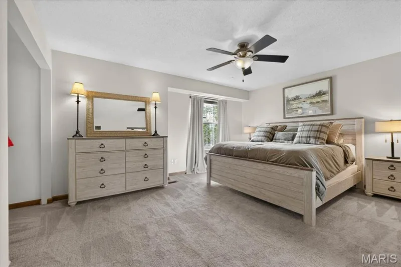 Plush carpeted flooring, a ceiling fan with integrated lighting, and a large window with privacy drapes — 1383 Forest Creek Drive #5, St Charles, MO 63303