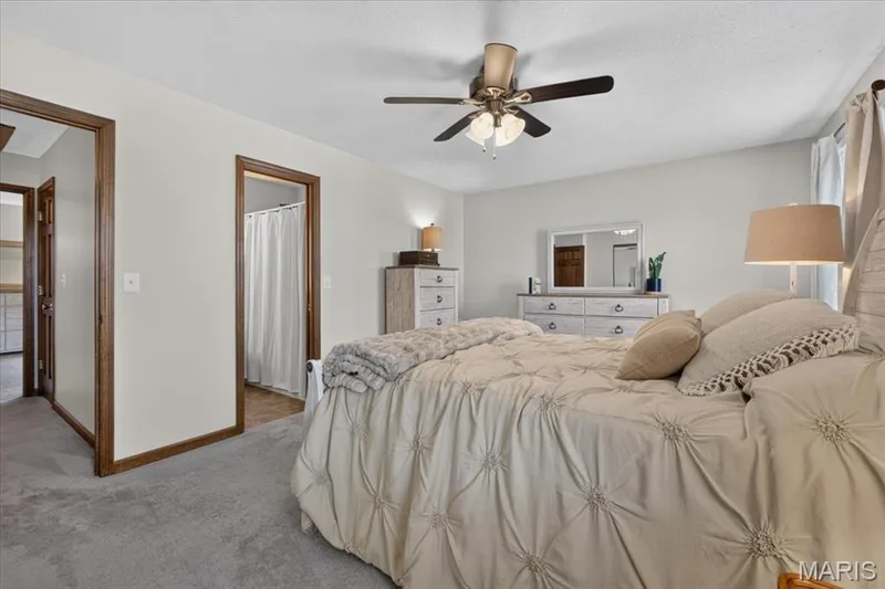 Bedroom featuring neutral wall colors, carpet flooring, a ceiling fan with integrated lighting, and multiple doorways with wood trim — 1383 Forest Creek Drive #5, St Charles, MO 63303