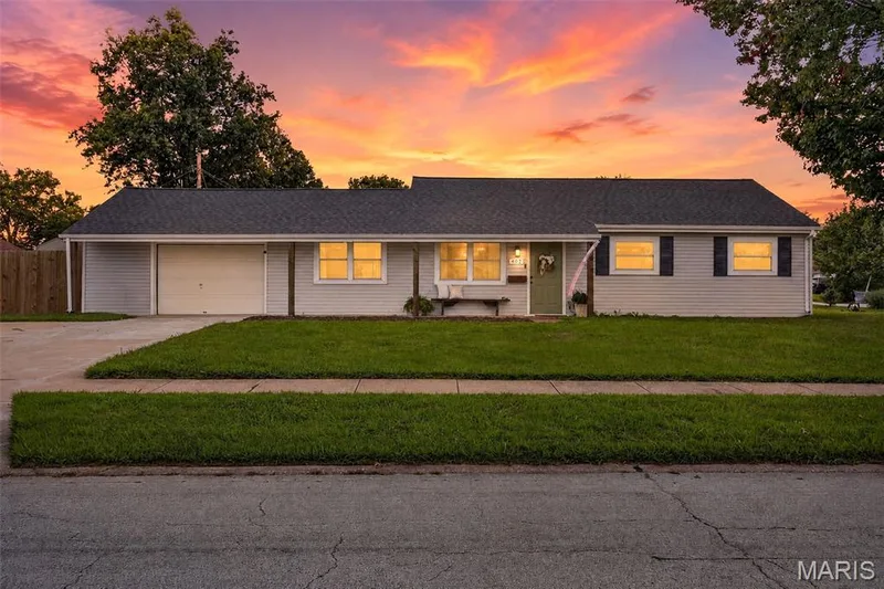 Single-story residence featuring light-colored siding, a dark shingle roof, a front-facing garage, and a concrete driveway — 402 Saint Joseph Avenue, St Charles, MO 63366