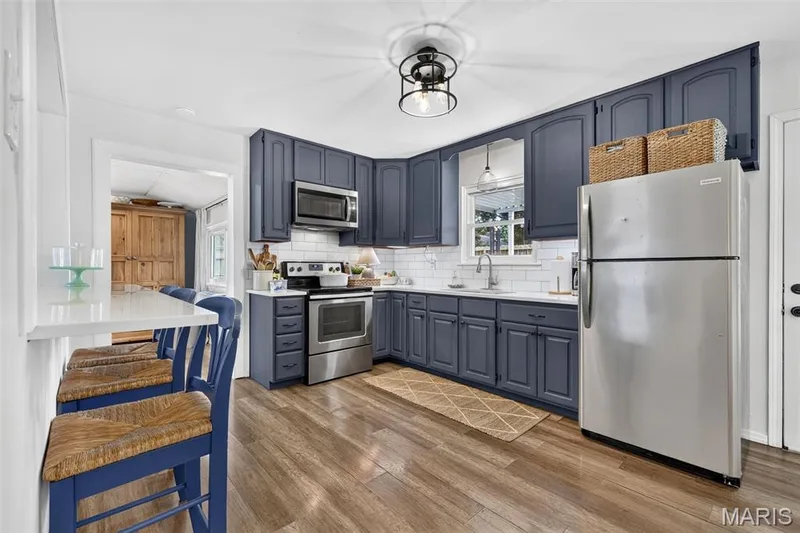 Kitchen featuring wood-finish flooring, white subway tile backsplash, stainless steel appliances, blue cabinetry, and a white countertop with a breakfast bar — 402 Saint Joseph Avenue, St Charles, MO 63366
