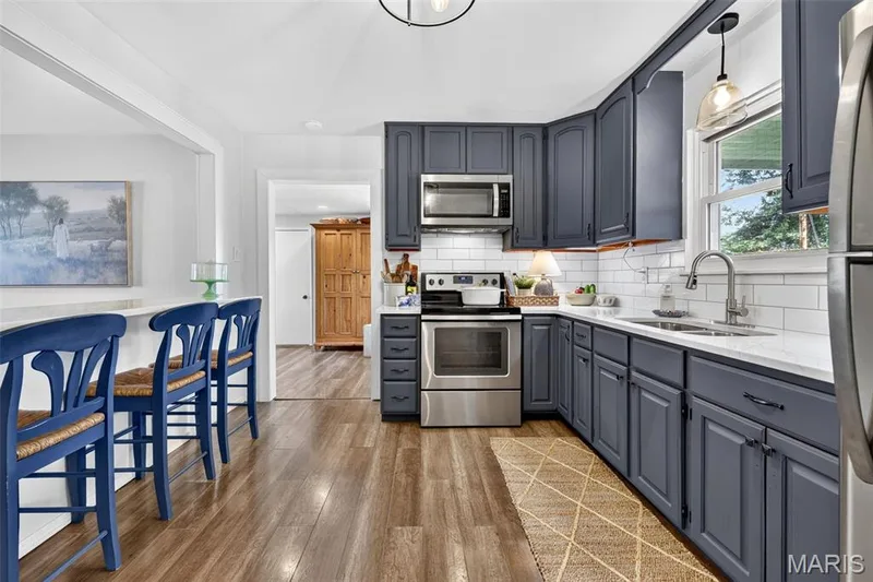 Kitchen featuring wood-finish flooring, white subway tile backsplash, stainless steel appliances, white countertops, and dark gray cabinetry — 402 Saint Joseph Avenue, St Charles, MO 63366