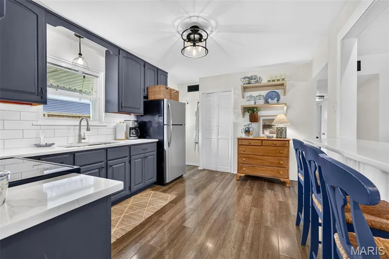 Kitchen featuring dark blue cabinetry, white subway tile backsplash, white countertops, wood-finish flooring, and stainless steel appliances — 402 Saint Joseph Avenue, St Charles, MO 63366