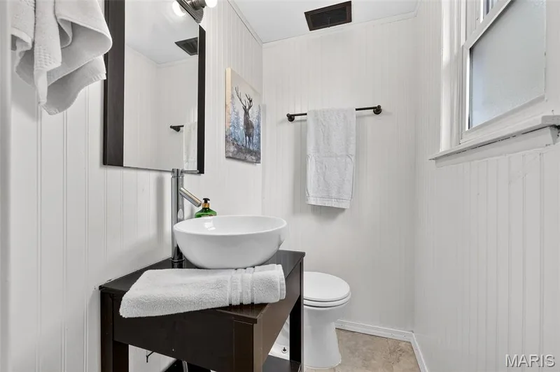 White beadboard paneling, vessel sink, dark wood-finish vanity, wall-mounted mirror, and a window providing natural light — 402 Saint Joseph Avenue, St Charles, MO 63366