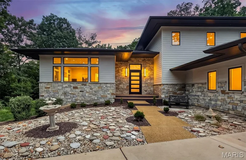 Modern architectural design featuring stone facade accents, large picture windows, and a distinctive entry door — 19256 Saint Albans Forest Lane, Wildwood, MO 63038