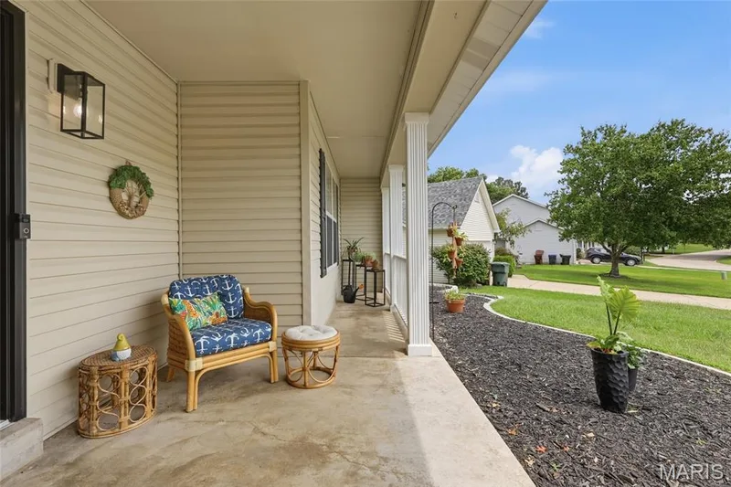 Covered front porch with concrete flooring, fluted columns, and exterior wall lantern — 1094 Treeshade Drive, St Peters, MO 63376