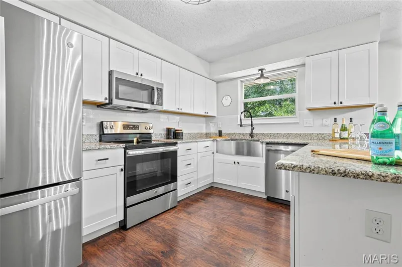 White cabinetry with black hardware, wood-finish flooring, stainless steel appliances, granite countertops, and a farmhouse-style sink — 1094 Treeshade Drive, St Peters, MO 63376