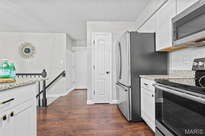 Wood-finish flooring throughout, white upper and lower cabinetry, light-toned granite-style countertops, stainless steel appliances, and a white subway tile backsplash — 1094 Treeshade Drive, St Peters, MO 63376