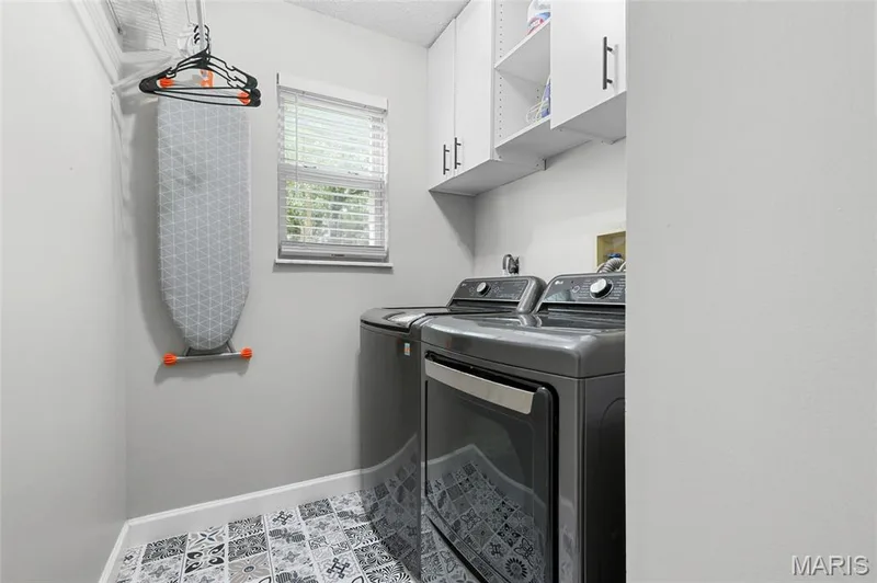 Laundry area with decorative floor tiling, window with blinds, and white upper cabinetry — 1094 Treeshade Drive, St Peters, MO 63376