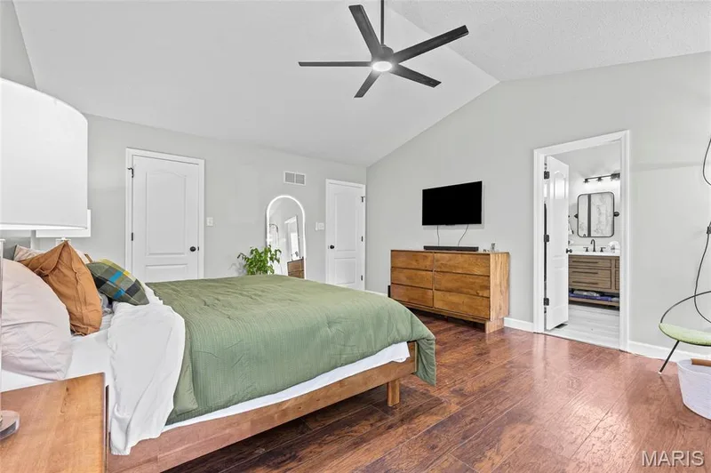 Vaulted ceiling with a modern ceiling fan, wood-finish flooring, and an adjoining bathroom featuring a vanity with an integrated sink and rectangular framed mirror — 1094 Treeshade Drive, St Peters, MO 63376