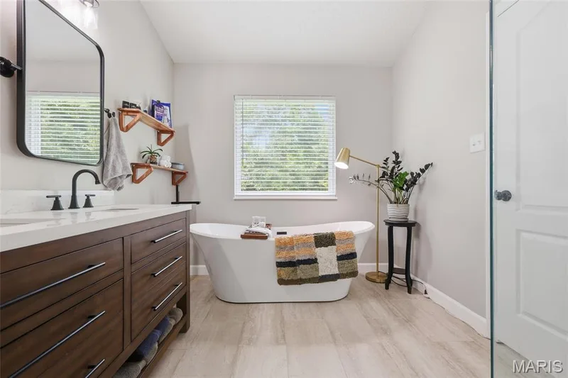 Freestanding soaking tub, wood-finish flooring, dual-sink vanity with white countertop, matte black fixtures, and a glass-enclosed shower — 1094 Treeshade Drive, St Peters, MO 63376