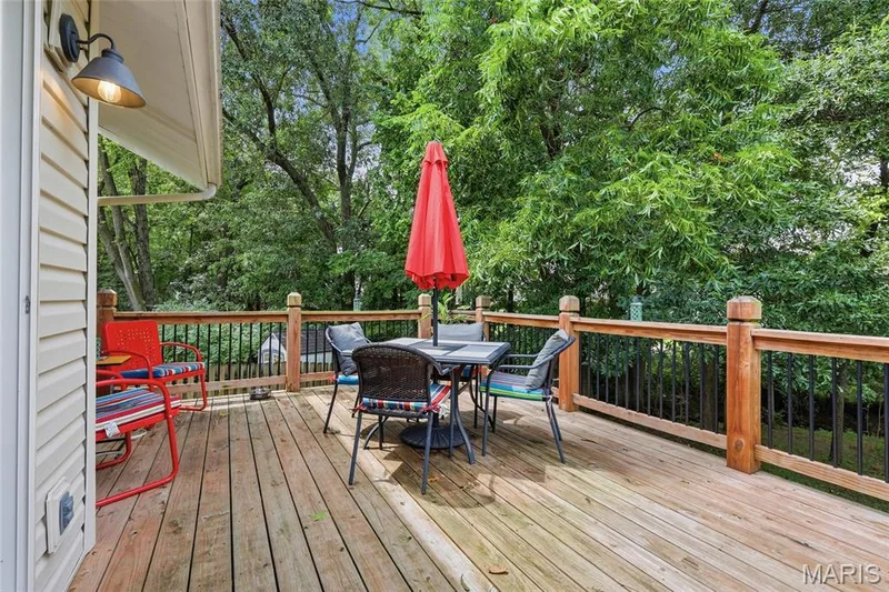 Wood deck with natural wood railings, black metal balusters, and exterior wall light fixture — 1094 Treeshade Drive, St Peters, MO 63376