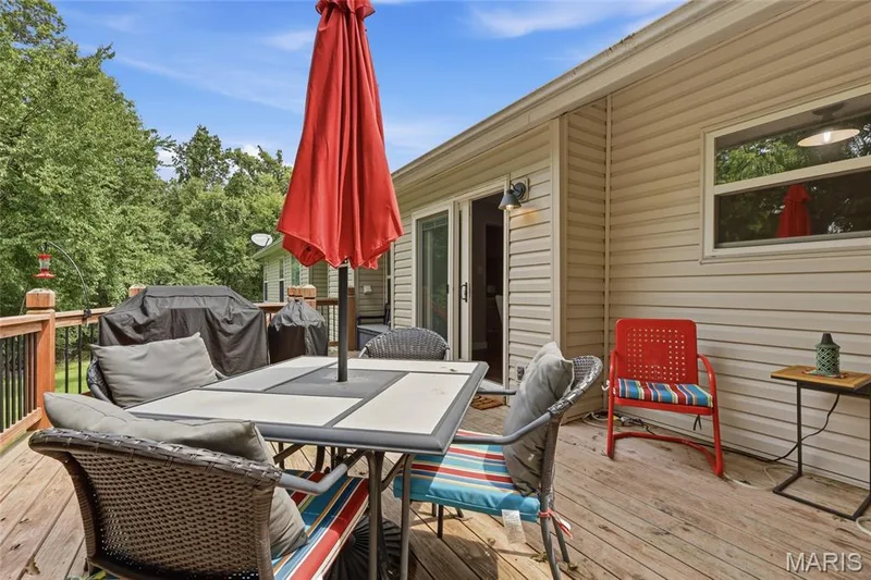 Expansive wood deck with black metal railing, featuring a sliding glass door and exterior wall sconce — 1094 Treeshade Drive, St Peters, MO 63376