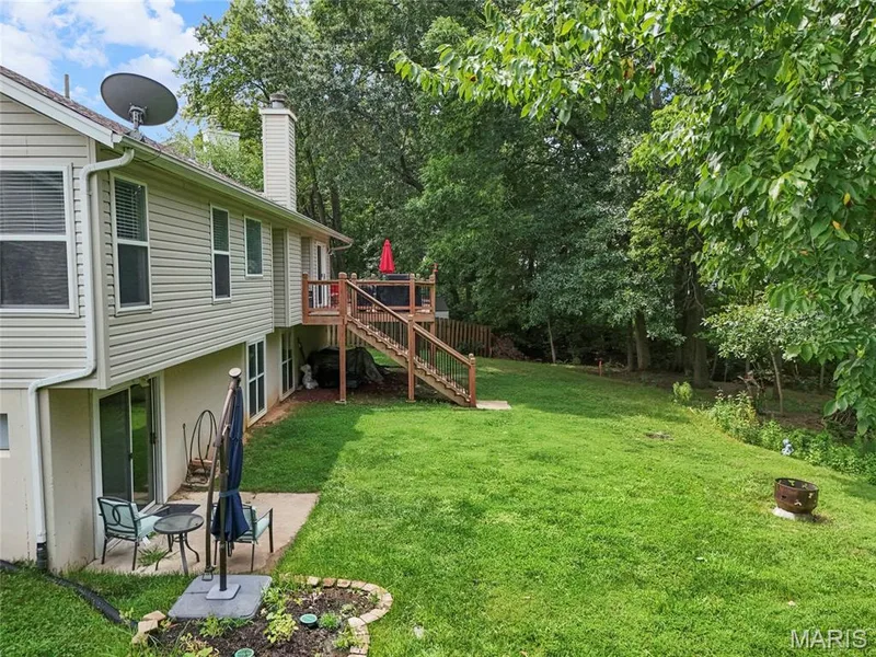 Expansive backyard with a manicured lawn, multi-level wooden deck, and concrete patio — 1094 Treeshade Drive, St Peters, MO 63376