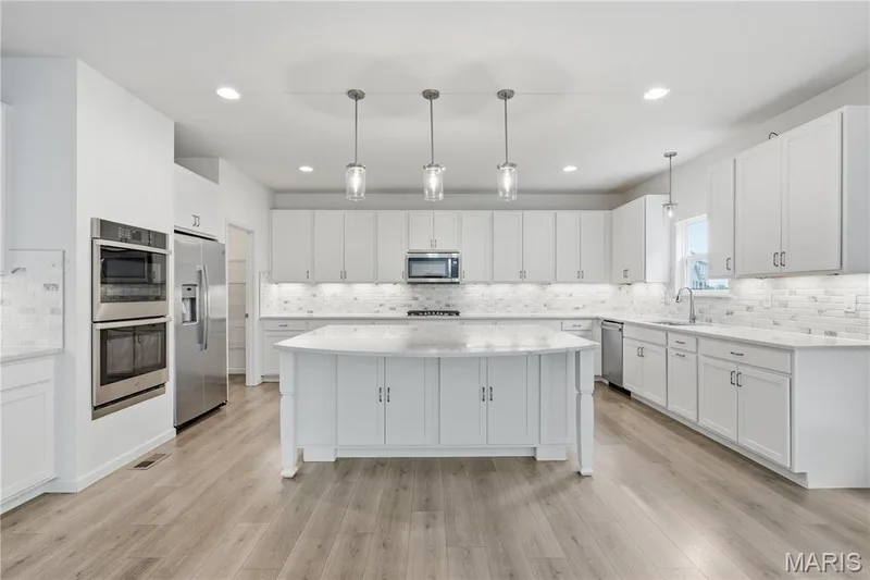 Designer kitchen with upgraded 42" white Shaker cabinetry, Helix quartz countertops, marble subway tile backsplash, under cabinet lighting, large walk-in pantry, premium stainless appliances, and a 7' center island. — 1278 Harvester Drive, Chesterfield, MO 63005