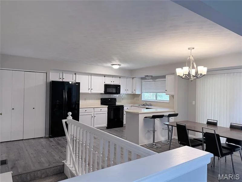Kitchen featuring white cabinetry, black appliances, a breakfast bar, and wood-finish flooring — 21 White Chapel, O'Fallon, MO 63368