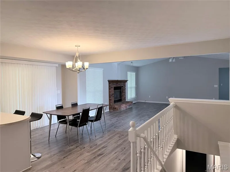 Open-concept living area with wood-finish flooring, a brick fireplace, and vaulted ceilings — 21 White Chapel, O'Fallon, MO 63368