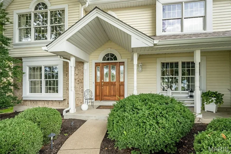 Exterior featuring light-colored siding, brick accents, a covered entry, and a wood-paneled double door with an arched transom — 1551 Country Bend Drive, St Charles, MO 63303