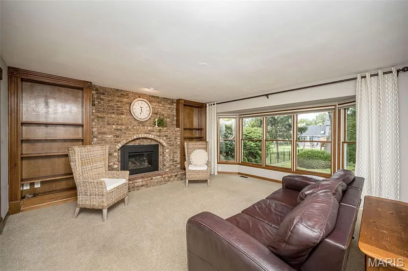 Brick fireplace with an arched hearth, built-in shelving, bay windows, and neutral carpet flooring — 1551 Country Bend Drive, St Charles, MO 63303