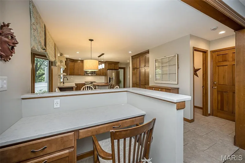 Built-in desk area with a light-toned countertop, wood-finish cabinetry, and a kitchen visible beyond — 1551 Country Bend Drive, St Charles, MO 63303