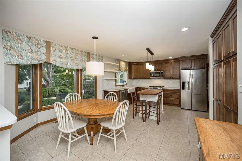 Kitchen featuring wood cabinetry, stainless steel appliances, a center island with seating, a ceramic tile backsplash, and a large bay window — 1551 Country Bend Drive, St Charles, MO 63303