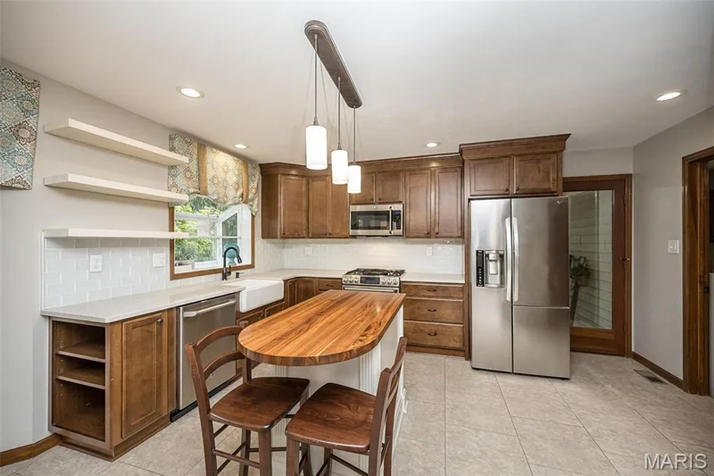 Wood cabinetry with stainless steel appliances, white subway tile backsplash, white farmhouse sink, wood-finish island countertop, and tiled flooring — 1551 Country Bend Drive, St Charles, MO 63303