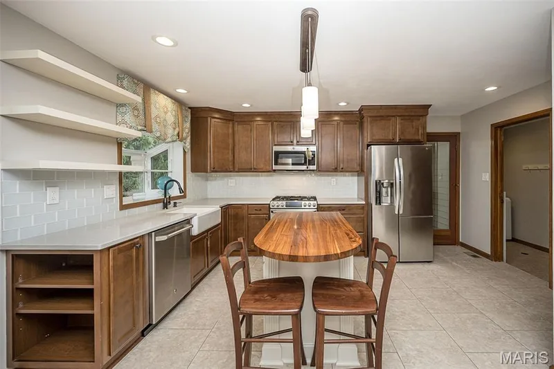Kitchen featuring wood cabinetry, stainless steel appliances, white subway tile backsplash, farmhouse sink, and a center island with a wood-finish countertop — 1551 Country Bend Drive, St Charles, MO 63303