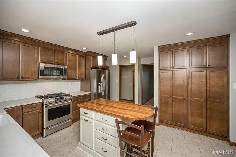 Wood-finish cabinetry with crown molding, stainless steel appliances, white subway tile backsplash, light-colored countertops, and a center island with a wood-finish top — 1551 Country Bend Drive, St Charles, MO 63303