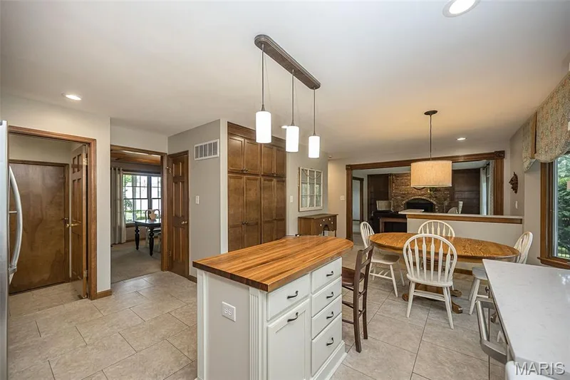 Spacious kitchen featuring an island with a wood-finish countertop, extensive built-in cabinetry, tile flooring, recessed lighting, and a window with a valance — 1551 Country Bend Drive, St Charles, MO 63303