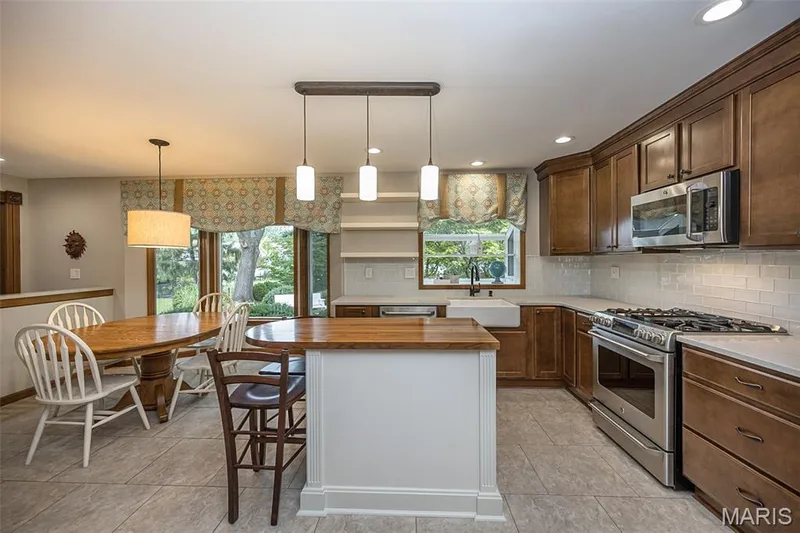 Spacious kitchen featuring warm wood cabinetry, stainless steel appliances, a large farmhouse sink, a breakfast bar, and recessed lighting — 1551 Country Bend Drive, St Charles, MO 63303