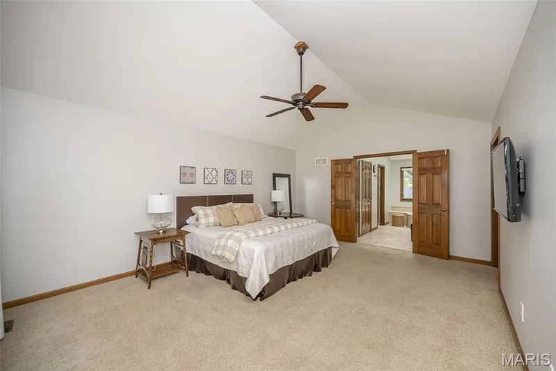 Vaulted ceiling with a ceiling fan, light-colored carpeting, warm-toned wood trim, and double doors opening to another space — 1551 Country Bend Drive, St Charles, MO 63303