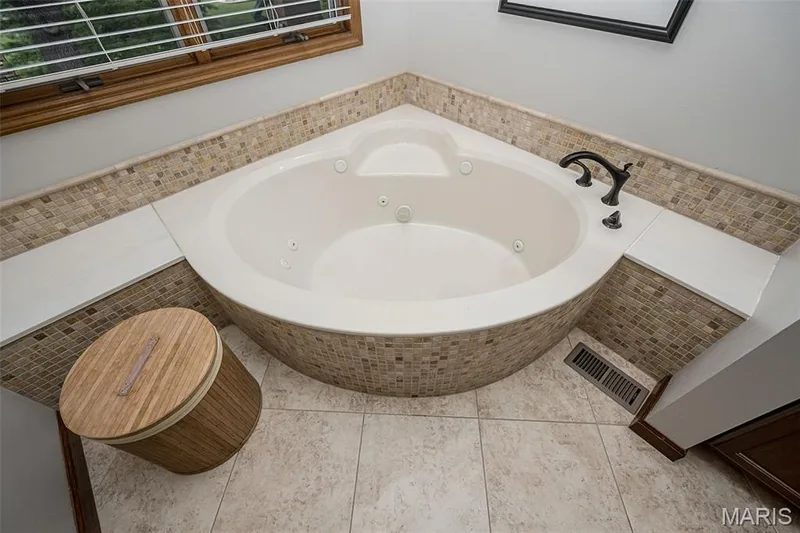 Corner jetted tub with mosaic tile surround, solid surface decking, and bronze fixtures — 1551 Country Bend Drive, St Charles, MO 63303