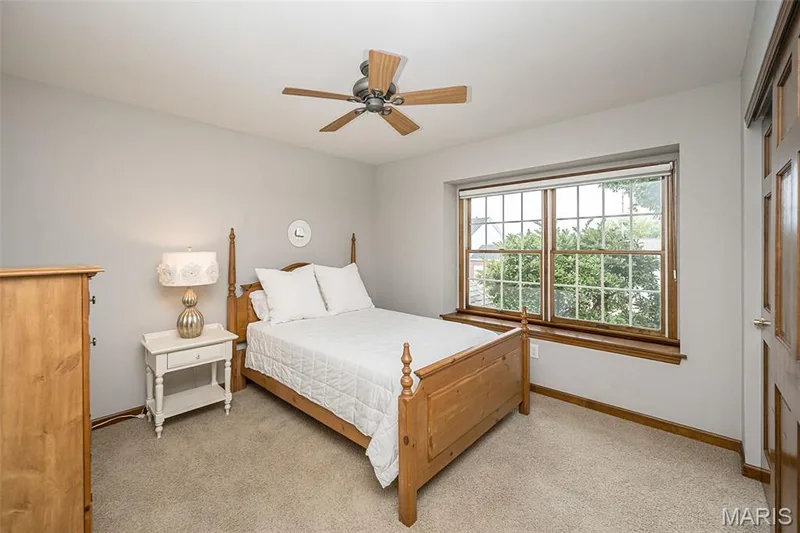 Ceiling fan with wooden blades, light gray painted walls, a large window with wooden trim, and light-colored carpeting — 1551 Country Bend Drive, St Charles, MO 63303