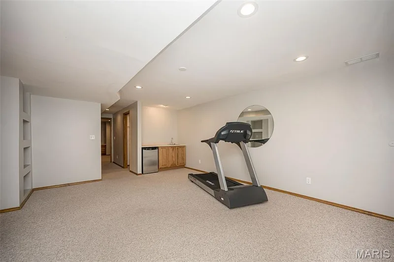 Recessed lighting illuminates a spacious room featuring a built-in wet bar with wood cabinetry and stainless steel undercounter refrigerator — 1551 Country Bend Drive, St Charles, MO 63303