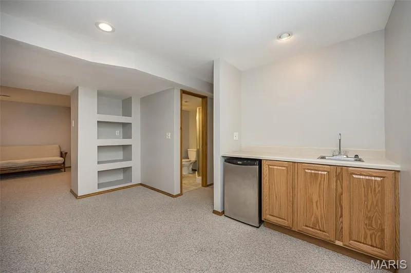 Wet bar with wood cabinetry and stainless steel undercounter refrigerator, built-in shelving, recessed lighting, and light-toned carpeting — 1551 Country Bend Drive, St Charles, MO 63303