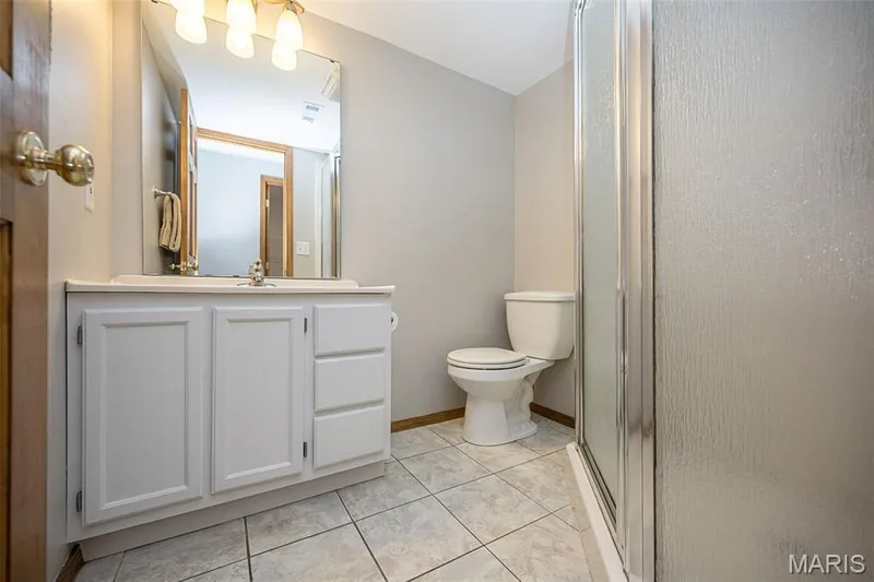 Full bathroom featuring a white vanity with integrated sink, overhead lighting, a glass-enclosed shower, and tile flooring — 1551 Country Bend Drive, St Charles, MO 63303