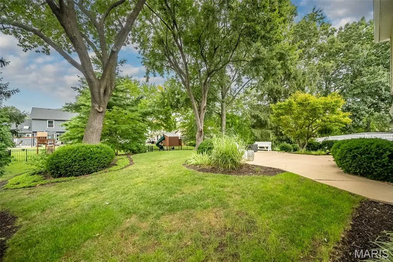 Expansive lawn area with mature trees, established landscaping, a concrete patio, and a white fence — 1551 Country Bend Drive, St Charles, MO 63303