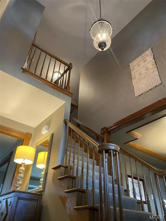 Carpeted staircase with wood railings, suspended light fixture, and a decorative wall hanging — 1551 Country Bend Drive, St Charles, MO 63303