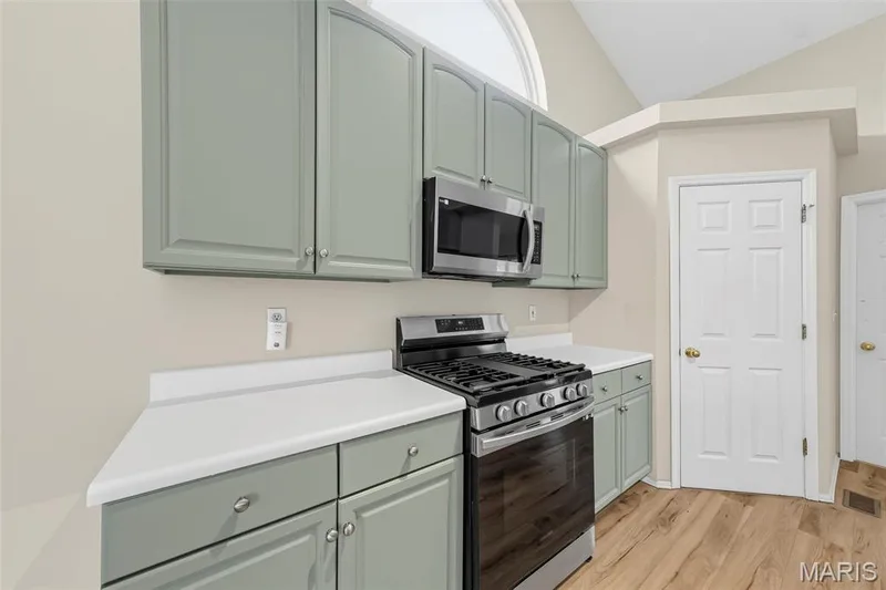 Kitchen featuring sage-toned cabinetry, stainless steel appliances, solid surface countertops, and wood-finish flooring — 934 Annabrook Park Drive, O'Fallon, MO 63366