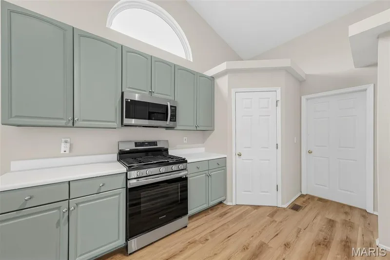 Contemporary kitchen featuring light green cabinetry, white countertops, stainless steel appliances, and wood-finish flooring — 934 Annabrook Park Drive, O'Fallon, MO 63366
