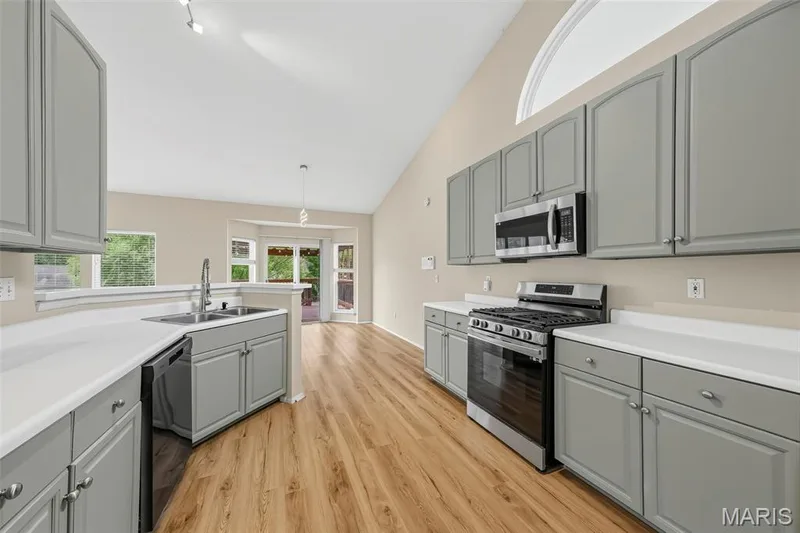 Kitchen featuring gray cabinetry, white countertops, stainless steel appliances, wood-finish flooring, and a vaulted ceiling — 934 Annabrook Park Drive, O'Fallon, MO 63366