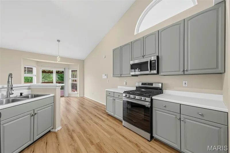 Vaulted ceiling with an arched window, wood-finish flooring, stainless steel appliances, gray cabinetry, and a double basin sink — 934 Annabrook Park Drive, O'Fallon, MO 63366
