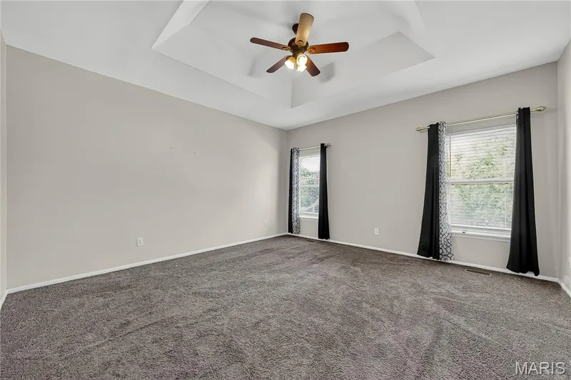 Spacious room featuring a tray ceiling, ceiling fan, and two windows — 934 Annabrook Park Drive, O'Fallon, MO 63366
